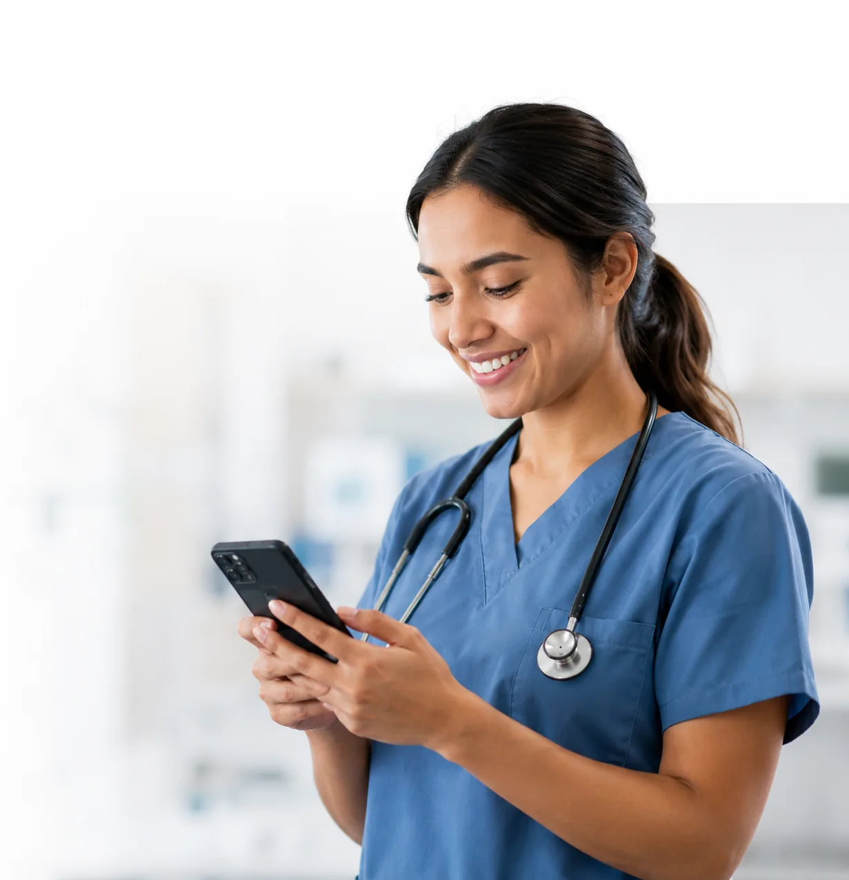 Nurse in scrubs smiling at a phone in a hospital corridor